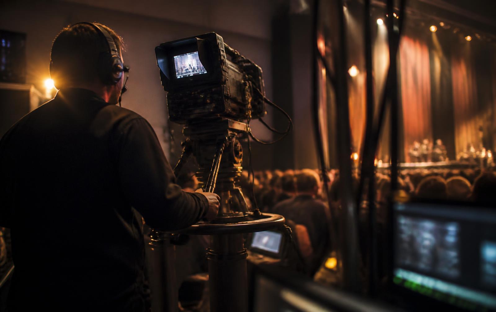 Camera operator working a broadcast camera at the side of a live stage